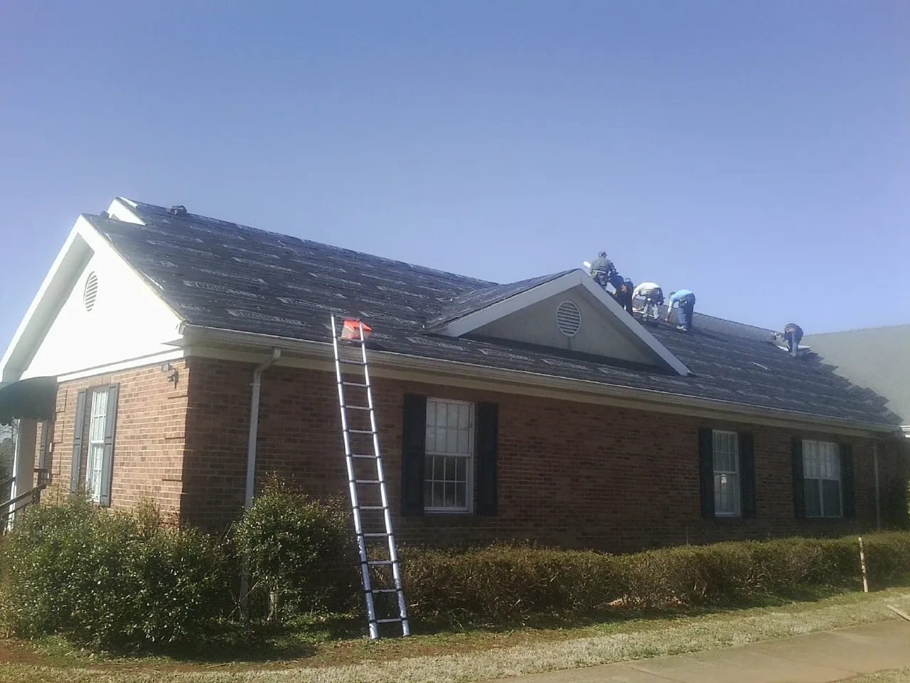 Crew tearing shingles off a brick ranch roof with a ladder set — Metal Roof Repair work by our crew in Forman