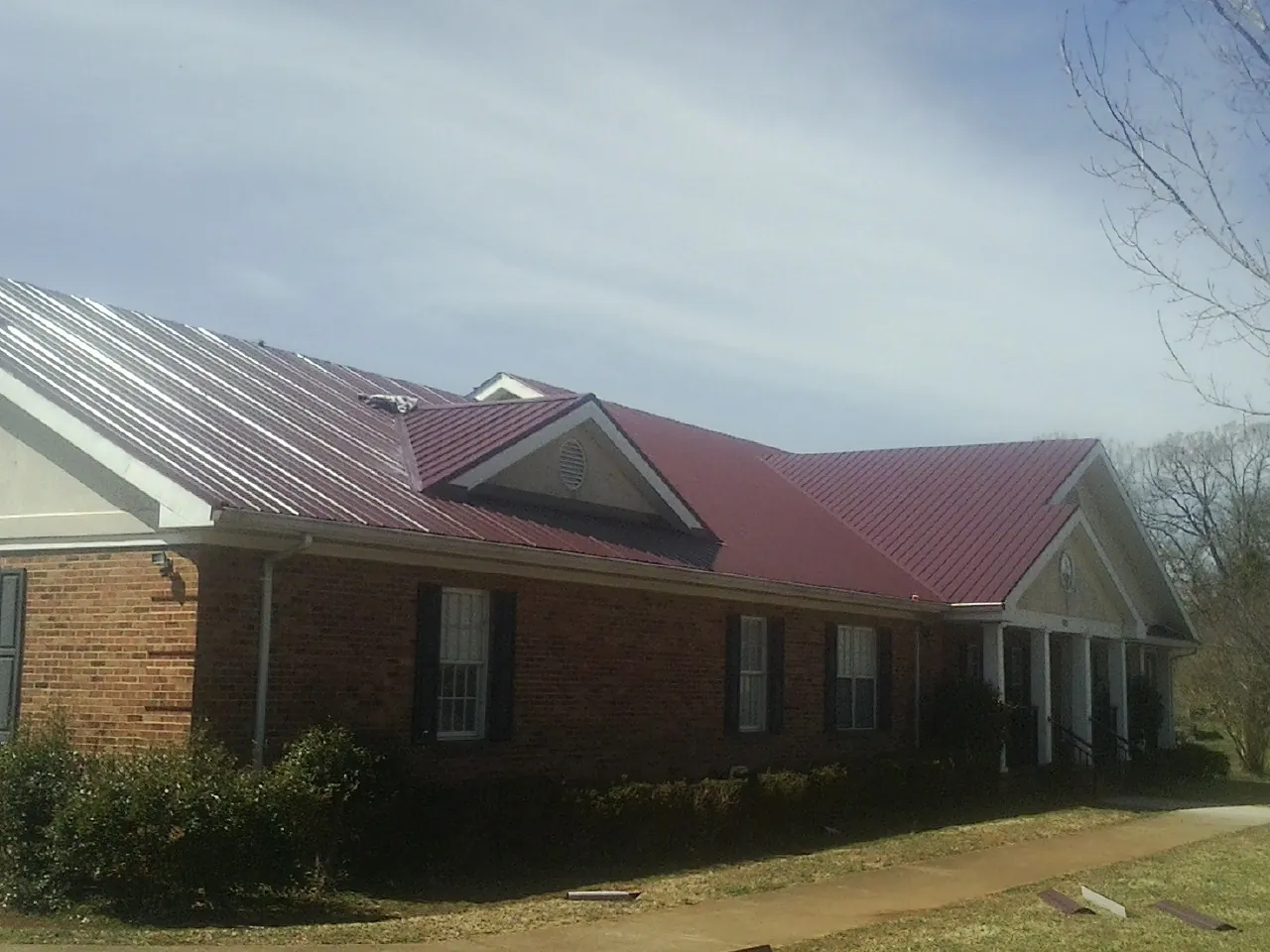 Red metal roof with gabled entries on a long brick building, from a Hail Damage Roof Repair job in Forman