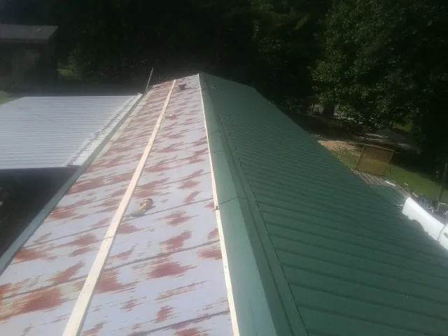 Old rusted panels beside newly installed green metal roofing — Wind Damage Roof Repair by Roofing Brothers in Forman