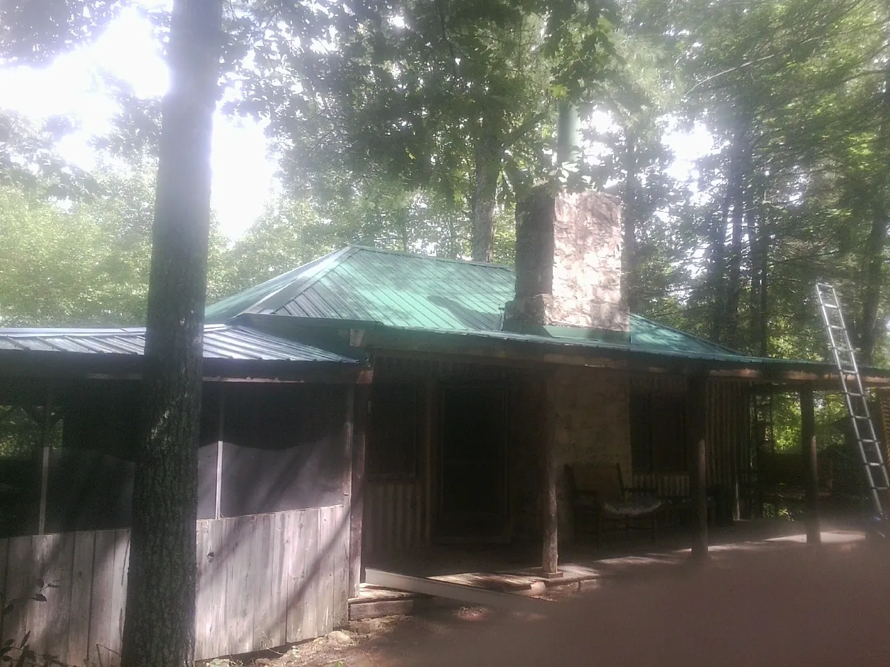 Green metal roof and stone chimney above a log cabin porch in Forman