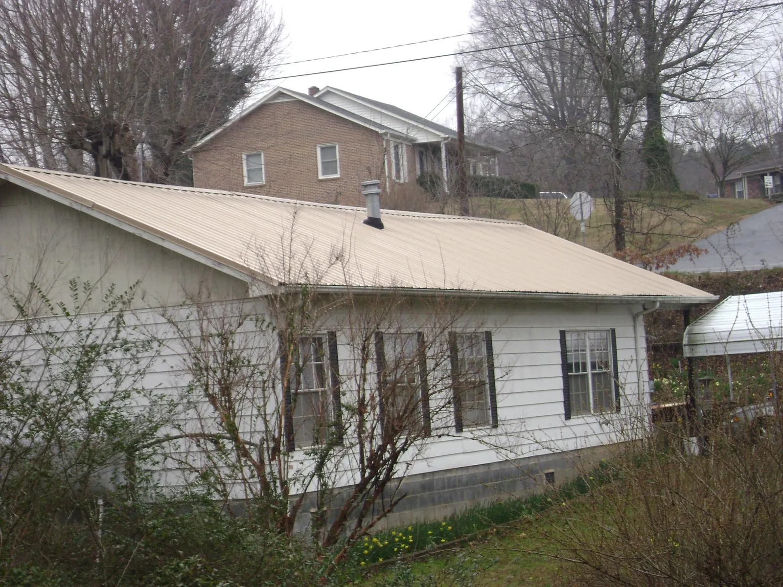 Tan metal roof on a white sided house set into a hillside — Commercial Roofing by Roofing Brothers in Forman