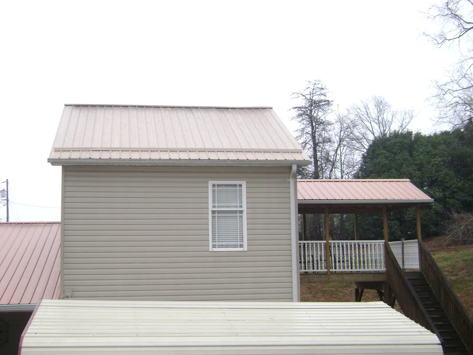 Tan metal roofs on a two story addition and attached porch, from a Roof Replacement job in Forman